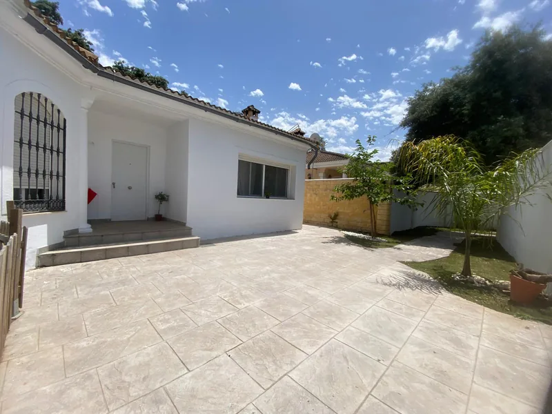 Casa blanca que aparece al fondo de un patio pavimentado