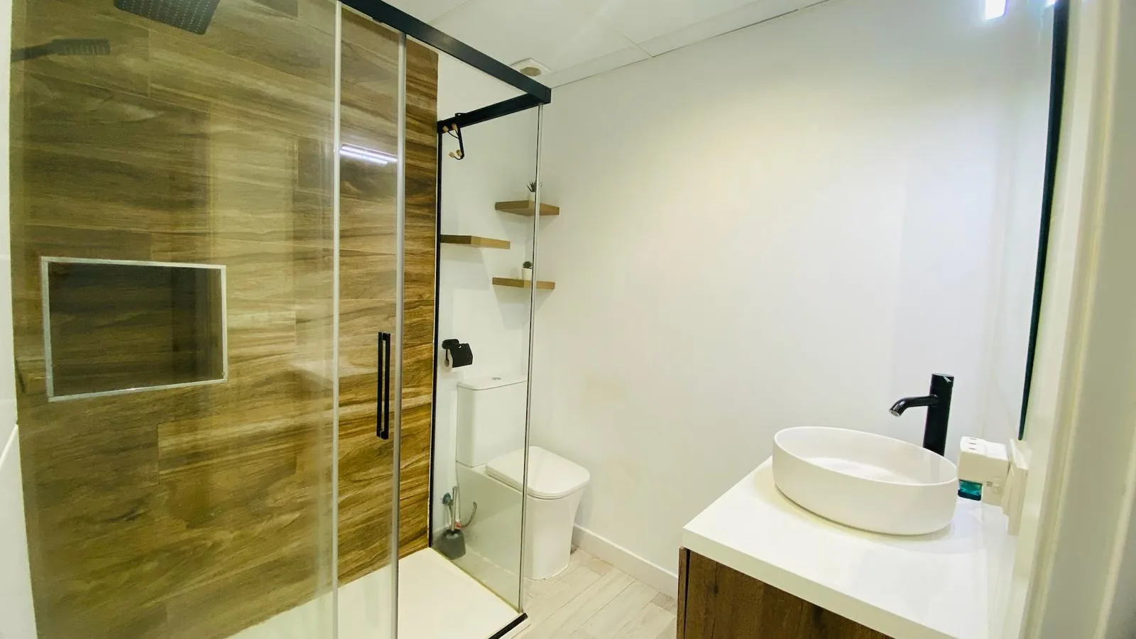 Baño blanco con ducha revestida en madera y mampara de vidrio