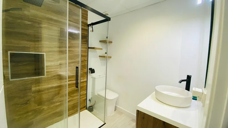 Baño blanco con ducha revestida en madera y mampara de vidrio