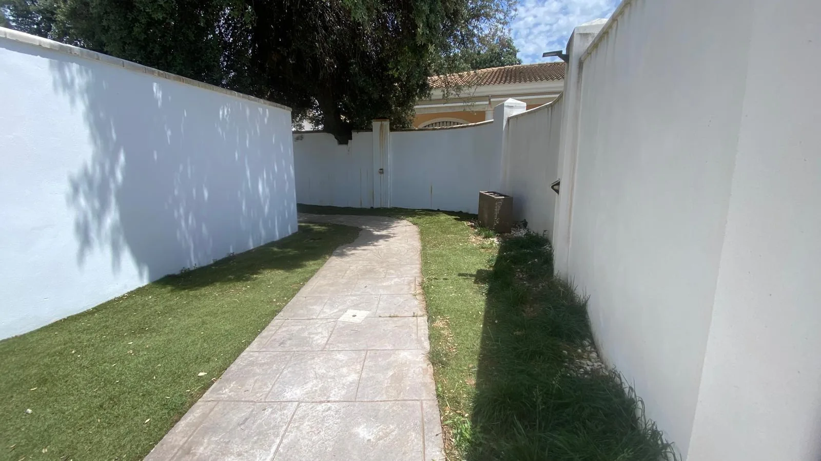Camino estrecho de pavimento entre césped y dos muros blancos
