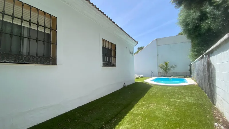 Fachada lateral con una franja de césped y la piscina al fondo