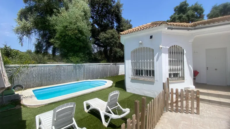 Piscina al fondo del jardín junto a la casa blanca y una cerca baja
